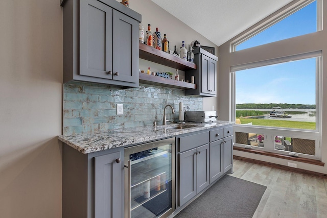 indoor wet bar featuring beverage cooler, lofted ceiling, backsplash, and light wood-style flooring