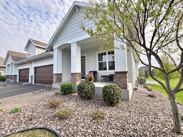 view of front of house with a porch, a garage, central air condition unit, and stone siding
