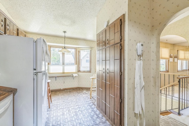 1567 Bavarian Pass, Fridley, MN 55432 - kitchen with freestanding refrigerator, wallpapered walls, arched walkways, brown cabinets, and a textured ceiling