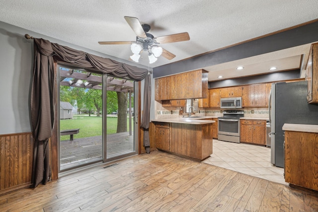 22800 401st Ave, Arlington Twp, MN 55307 - kitchen featuring appliances with stainless steel finishes, a peninsula, brown cabinets, light wood finished floors, and a ceiling fan