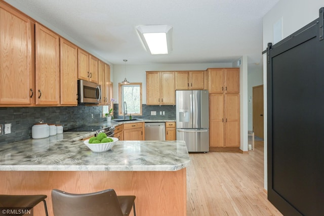 kitchen featuring stainless steel appliances, a peninsula, a sink, tasteful backsplash, and light wood-type flooring