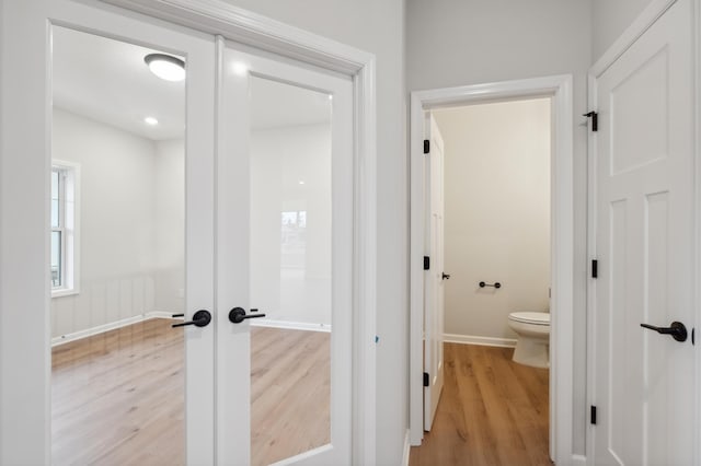 bathroom featuring wood finished floors, toilet, baseboards, and french doors