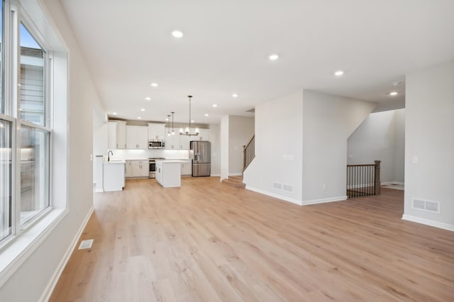 unfurnished living room with a sink, light wood-type flooring, baseboards, a chandelier, and recessed lighting