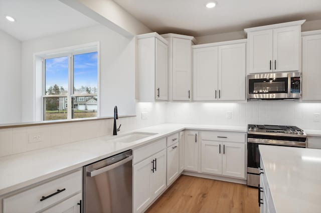 kitchen featuring appliances with stainless steel finishes, a sink, recessed lighting, decorative backsplash, and white cabinetry