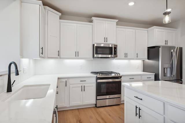 kitchen with stainless steel appliances, a sink, white cabinetry, light wood finished floors, and decorative backsplash
