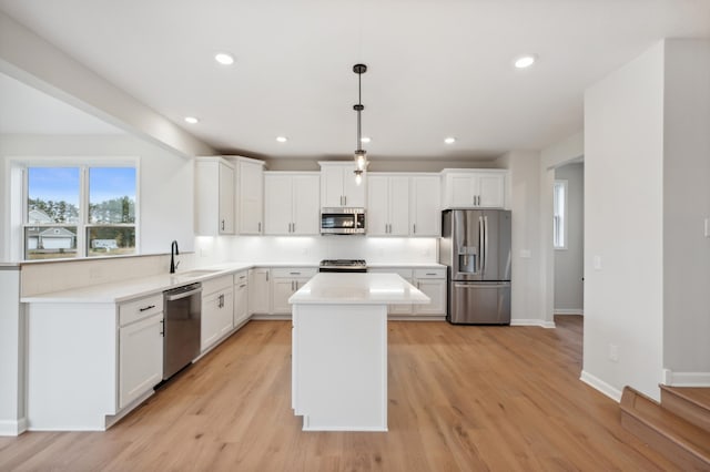 kitchen with appliances with stainless steel finishes, a sink, light wood-type flooring, a kitchen island, and recessed lighting