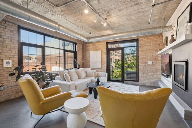 living area with brick wall, track lighting, concrete flooring, plenty of natural light, and a warm lit fireplace
