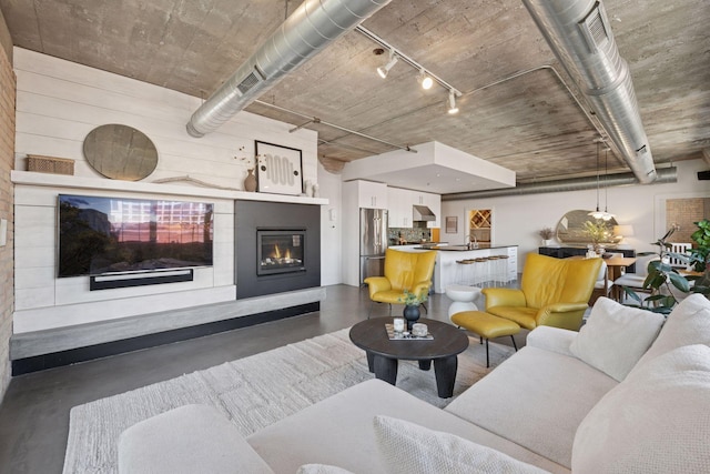 living room with concrete floors, track lighting, and a glass covered fireplace