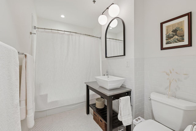 full bathroom featuring a sink, toilet, tile walls, a wainscoted wall, and shower / tub combo with curtain