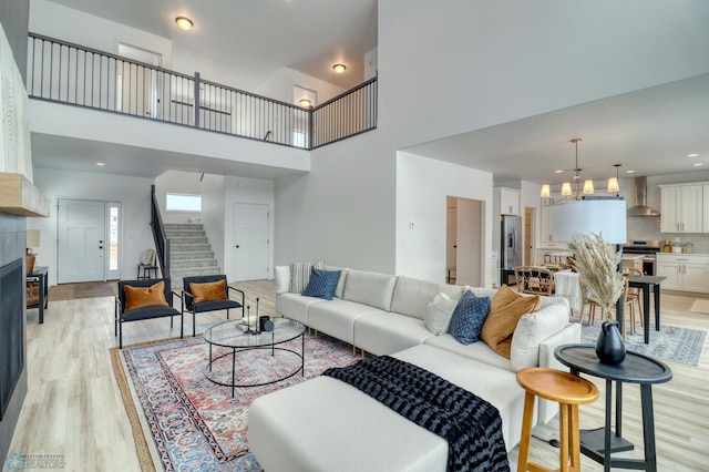 living room with stairs, light wood finished floors, a chandelier, and a high ceiling