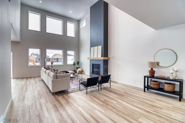 living room with wood finished floors, healthy amount of natural light, a fireplace, baseboards, and a towering ceiling