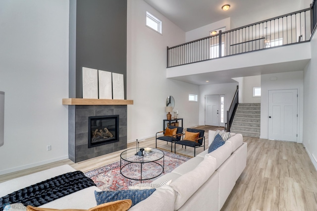living room featuring wood finished floors, stairway, a high ceiling, baseboards, and a fireplace