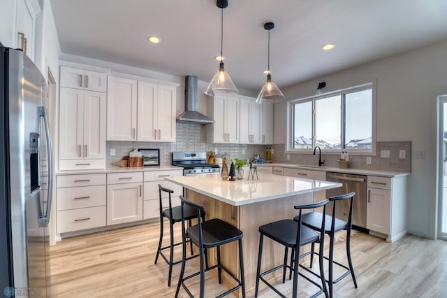 kitchen featuring appliances with stainless steel finishes, wall chimney range hood, light countertops, light wood-style floors, and recessed lighting