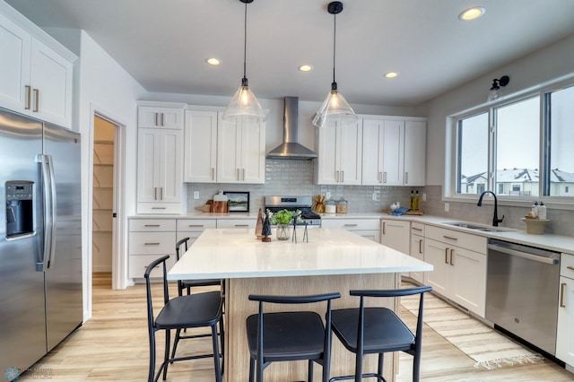 kitchen with stainless steel appliances, wall chimney range hood, a sink, a kitchen bar, and light countertops