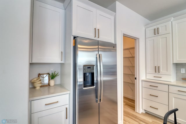 kitchen with stainless steel refrigerator with ice dispenser, light countertops, white cabinets, and light wood-style floors