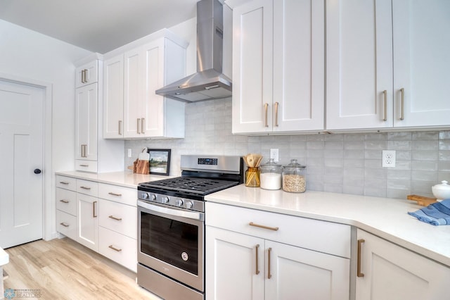 kitchen with stainless steel gas stove, wall chimney exhaust hood, light countertops, white cabinetry, and light wood-style floors