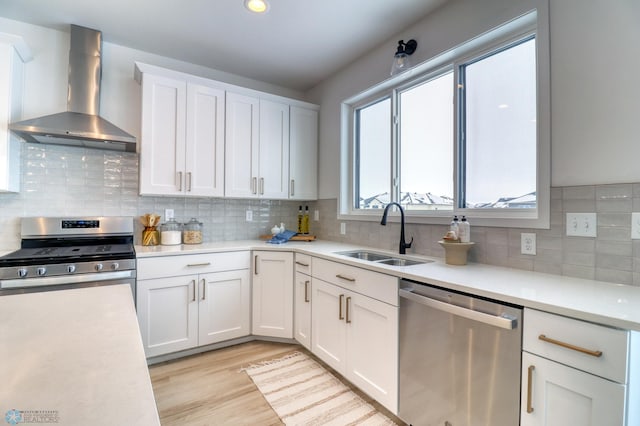 kitchen featuring stainless steel appliances, wall chimney range hood, a sink, light countertops, and white cabinetry