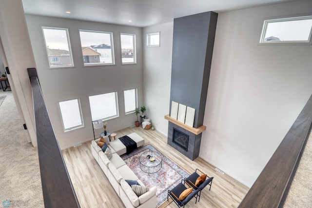 living area featuring a fireplace, wood finished floors, a towering ceiling, and recessed lighting