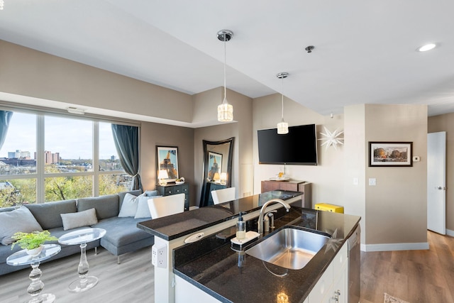 kitchen featuring a sink, light wood-type flooring, open floor plan, hanging light fixtures, and white cabinets