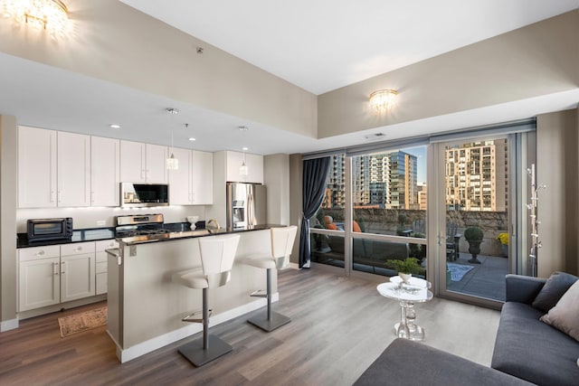 kitchen with stainless steel appliances, wood finished floors, dark countertops, white cabinetry, and recessed lighting