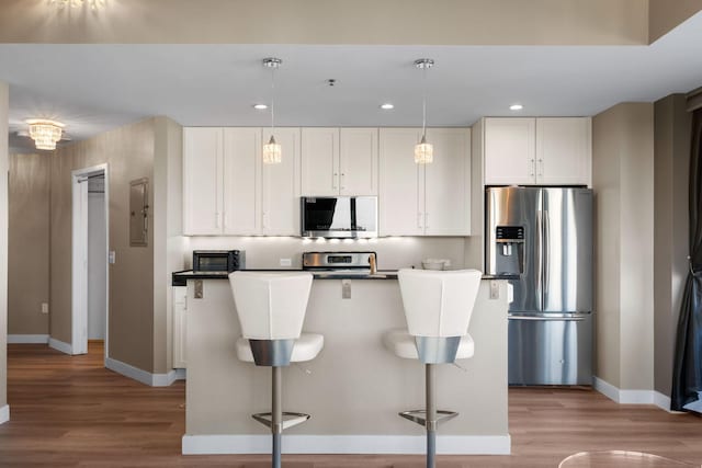 kitchen with stainless steel appliances, baseboards, light wood finished floors, white cabinetry, and a breakfast bar area