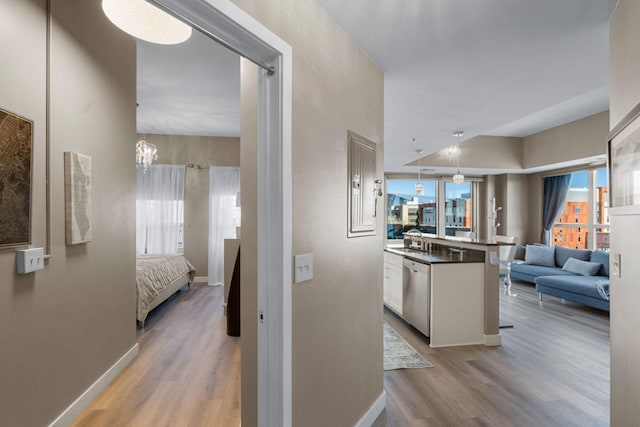 hall featuring light wood-type flooring, plenty of natural light, baseboards, and a chandelier
