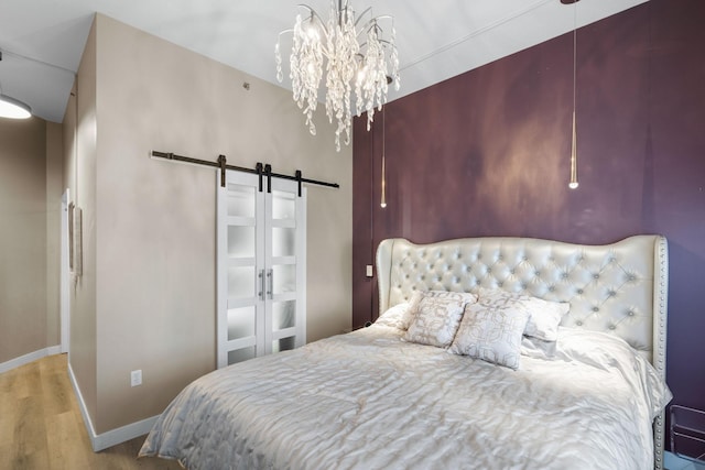 bedroom with a barn door, wood finished floors, baseboards, and a chandelier
