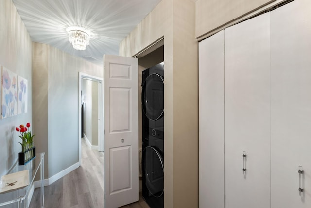 laundry room featuring estacked washer and dryer, light wood-type flooring, baseboards, and a chandelier