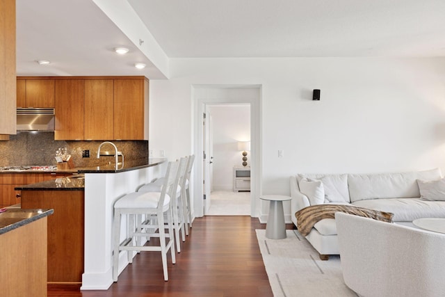 kitchen featuring brown cabinets, a kitchen bar, dark wood-style flooring, decorative backsplash, and open floor plan
