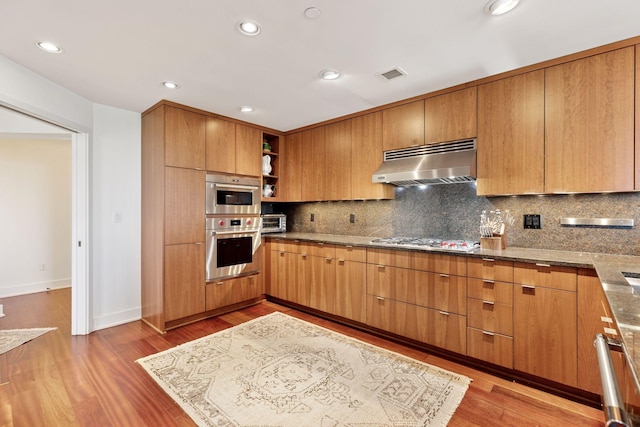 kitchen featuring under cabinet range hood, stainless steel gas cooktop, open shelves, decorative backsplash, and light wood-type flooring