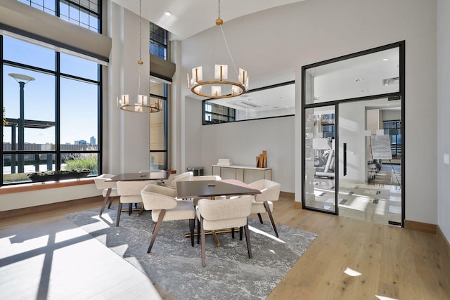 dining space featuring a chandelier, plenty of natural light, a high ceiling, wood finished floors, and baseboards