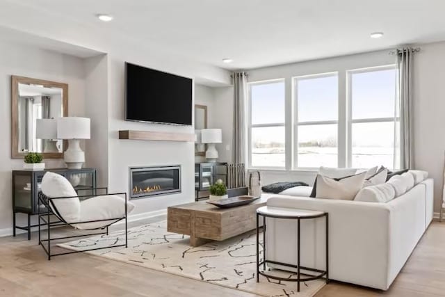 living room with wood finished floors, baseboards, a glass covered fireplace, and recessed lighting