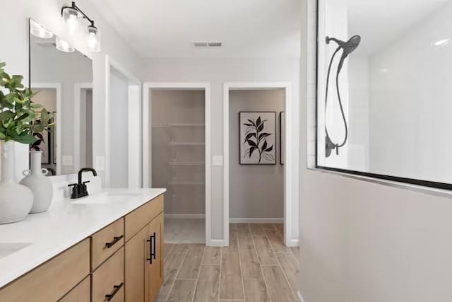full bathroom with a walk in closet, double vanity, wood finished floors, and baseboards