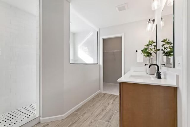 full bath featuring a tile shower, double vanity, wood finished floors, a walk in closet, and baseboards