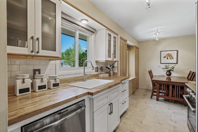 kitchen featuring wooden counters, stainless steel dishwasher, a sink, tasteful backsplash, and white cabinets
