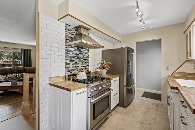 kitchen with wooden counters, stainless steel appliances, wall chimney exhaust hood, and decorative backsplash