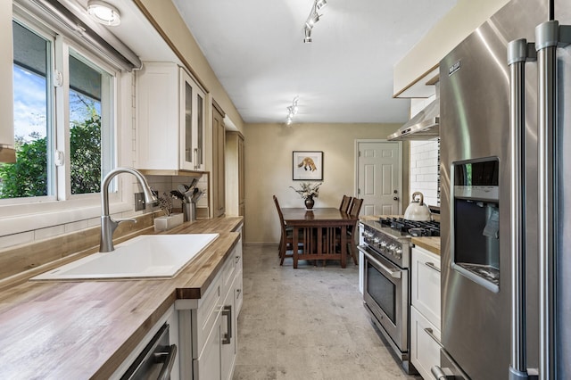 kitchen featuring appliances with stainless steel finishes, butcher block countertops, a sink, decorative backsplash, and extractor fan