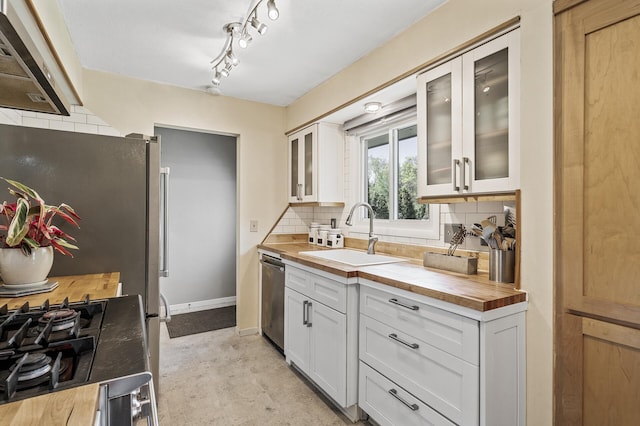 kitchen with a sink, wood counters, tasteful backsplash, appliances with stainless steel finishes, and wall chimney exhaust hood