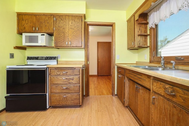 kitchen with electric range, white microwave, a sink, light wood-type flooring, and brown cabinets