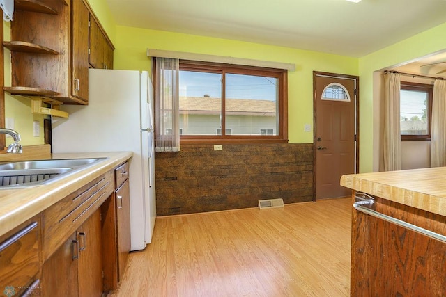 kitchen featuring a sink, light wood-style floors, open shelves, a wainscoted wall, and brown cabinetry