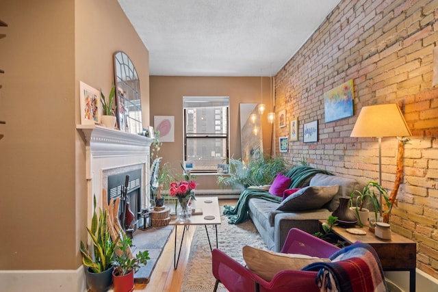 living area with a fireplace with raised hearth, brick wall, wood finished floors, and baseboards