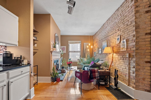 living area featuring light wood-type flooring, brick wall, a fireplace, a textured ceiling, and baseboards