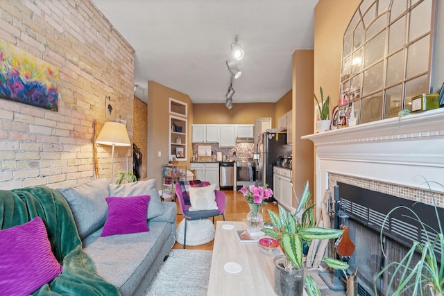 living room with light wood finished floors, brick wall, and a tile fireplace