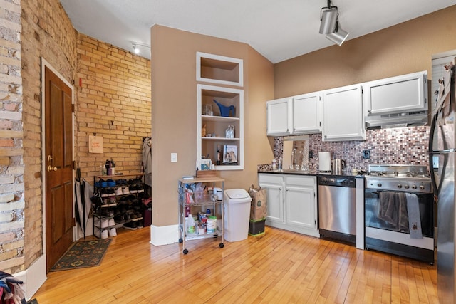 kitchen featuring stainless steel appliances, under cabinet range hood, white cabinets, light wood-style flooring, and brick wall