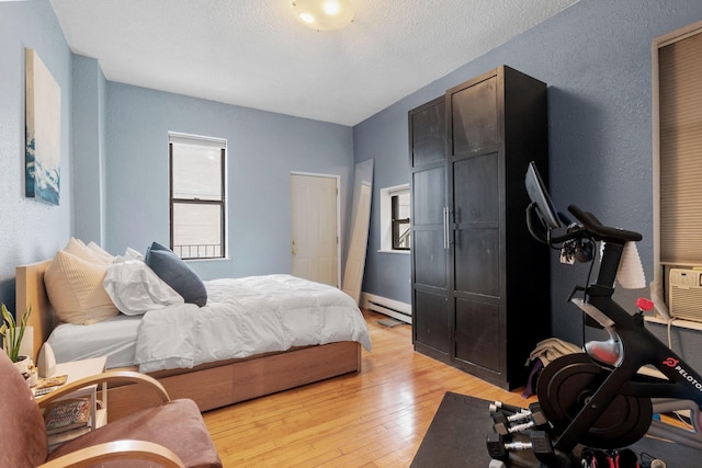bedroom featuring light wood-style floors, a baseboard radiator, and cooling unit