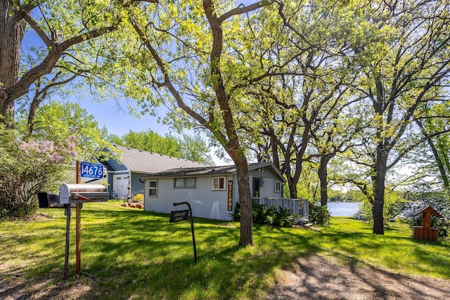 view of green lawn with a garage and a water view