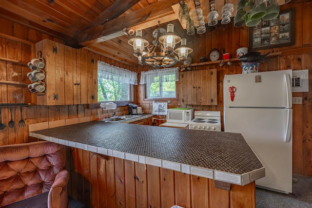 kitchen featuring white appliances, a sink, a peninsula, wooden walls, and carpet