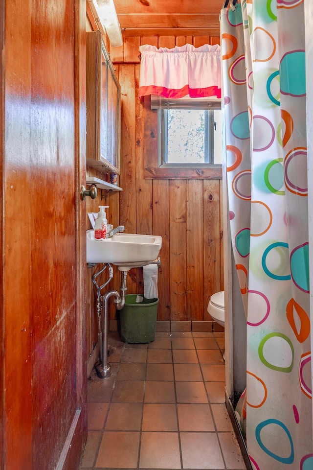 bathroom featuring a shower with curtain, wood walls, a sink, toilet, and tile patterned flooring