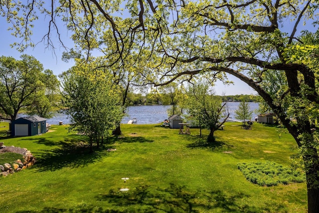 view of green lawn with a water view and an outbuilding