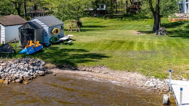 view of grassy yard featuring a shed, an outbuilding, and a water view